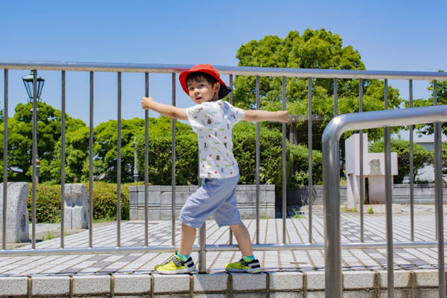 柵に掴まっている赤い帽子を被った男の子