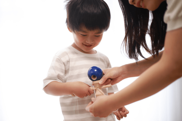 けん玉の持ち方を教える大人とそれを笑顔で持つ子ども